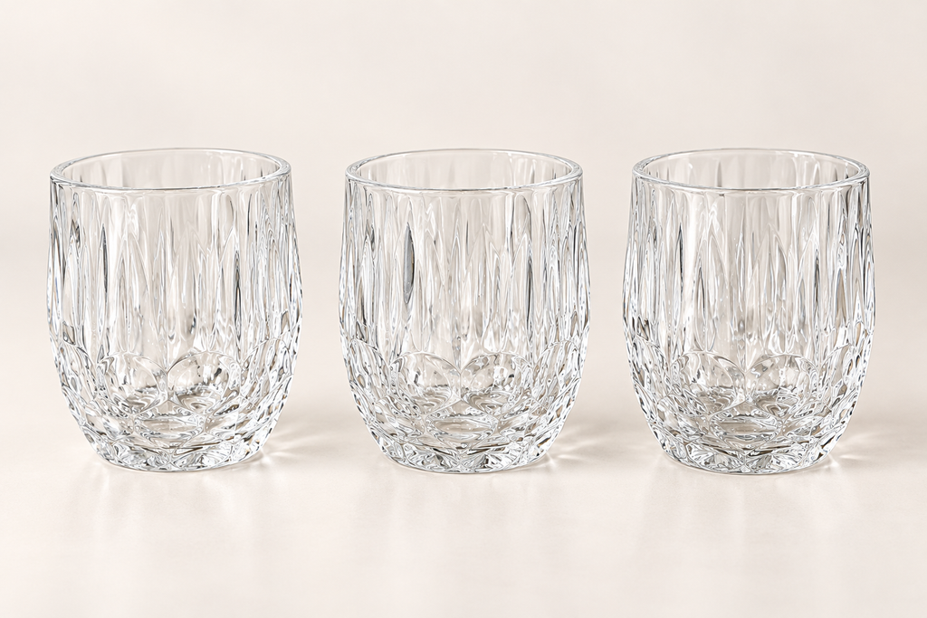 Three clear faceted glass tumblers on a neutral studio background